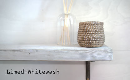 A limed-white painted wooden shelf with a woven basket candle holder and a clear glass reed diffuser bottle, set against a white textured wall. The text 'Limed-Whitewash' is visible in the bottom-left corner.