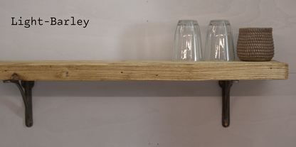 A light-barley wood floating shelf mounted on a wall with two dark metal brackets, styled with two clear drinking glasses and a woven basket, with the text 'Light-Barley' in the top left corner.