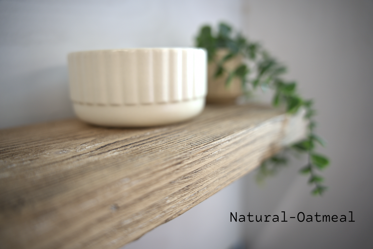 A small cream-colored ceramic bowl with a fluted exterior sits on a rustic wooden shelf, with a blurred green trailing plant in the background. The text 'Natural-Oatmeal' is printed in the bottom right corner.