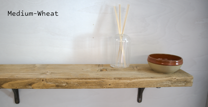 A rustic wooden shelf mounted on a white wall, styled with a clear glass reed diffuser bottle and a small beige and brown ceramic bowl. The text 'Medium-Wheat' is written in black typewriter font in the upper left corner.