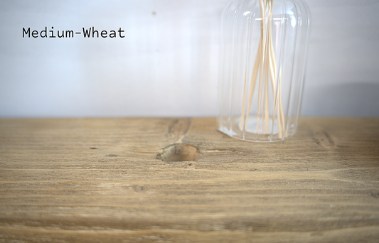 A close-up of a medium-wheat colored wood surface with a clear ribbed glass bottle containing thin wooden sticks, against a light neutral background. The text 'Medium-Wheat' is visible in the upper left.